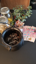 Load image into Gallery viewer, This is an image of my open cauldron with burning results, crystal money tree, ancestor money, jade tree, money oil, and money herbs.